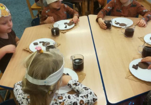 Dzieci siedzą przy stolikach smakują brązowe produkty.